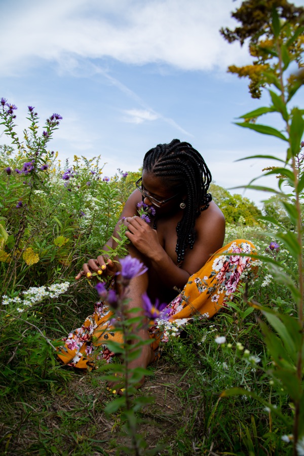 Tiffany Carey Jones seated among wildflowers, closely observing a single bloom